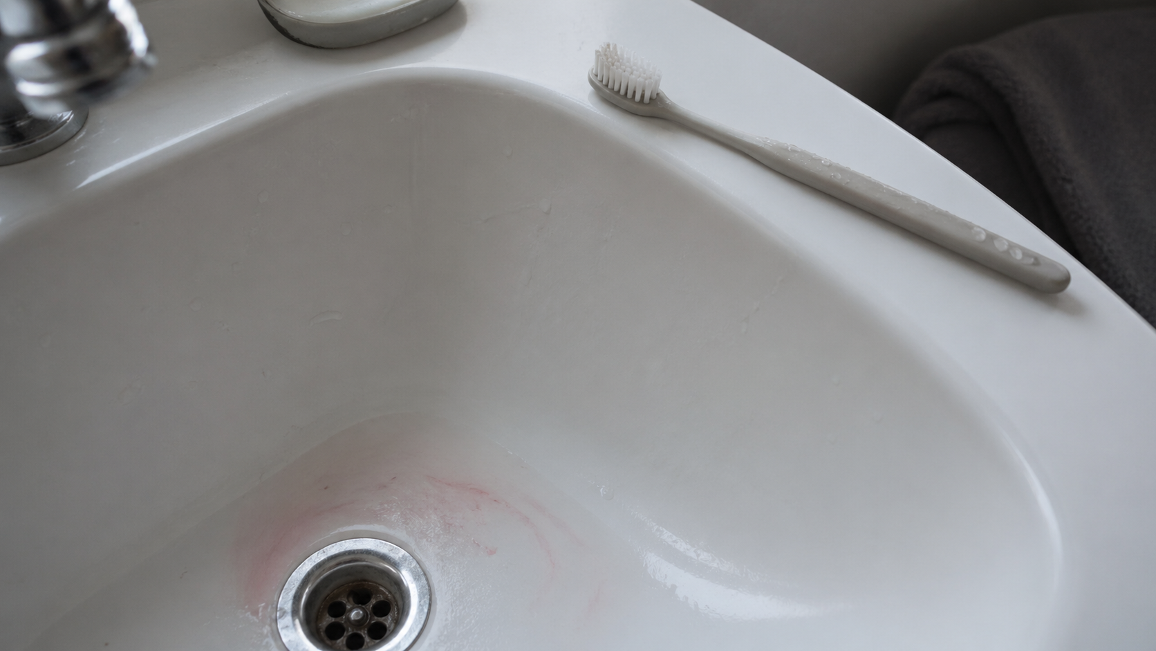 White porcelain sink with a toothbrush on the rim and faint pink residue in the drain